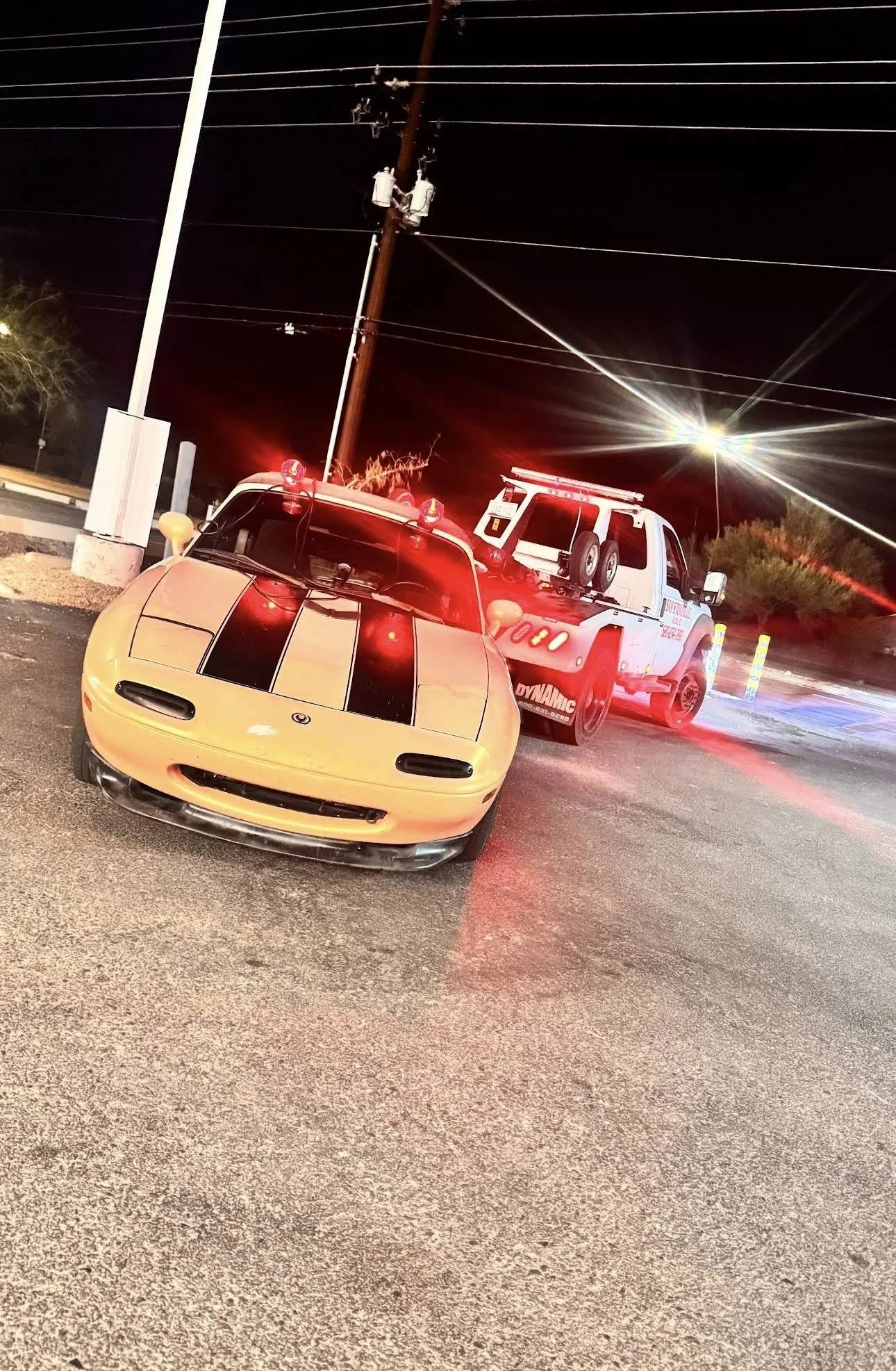 Sports car on a Tucson street at night beside a tow truck with flashing lights